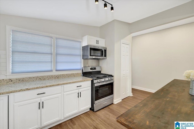 kitchen with stainless steel appliances, light hardwood / wood-style floors, white cabinets, and light stone countertops