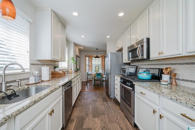 kitchen with light stone countertops, stainless steel appliances, dark wood-type flooring, sink, and white cabinetry