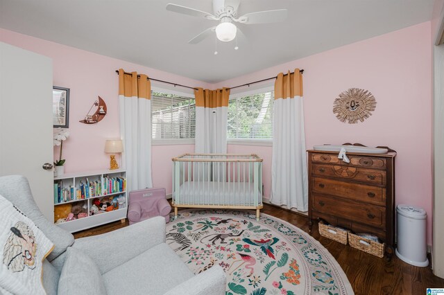 bedroom featuring ceiling fan, dark hardwood / wood-style flooring, and a crib