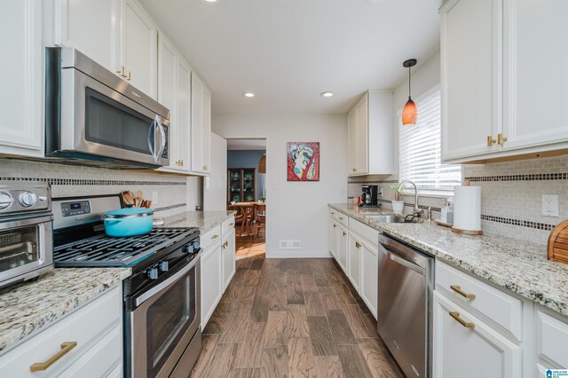 kitchen with pendant lighting, white cabinets, sink, appliances with stainless steel finishes, and dark hardwood / wood-style flooring