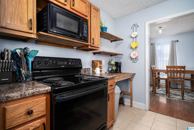 kitchen with light tile patterned flooring, a textured ceiling, dark stone countertops, and black appliances