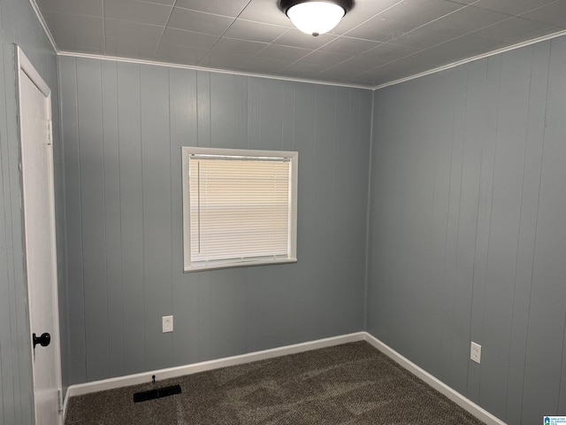 carpeted empty room featuring crown molding and wooden walls