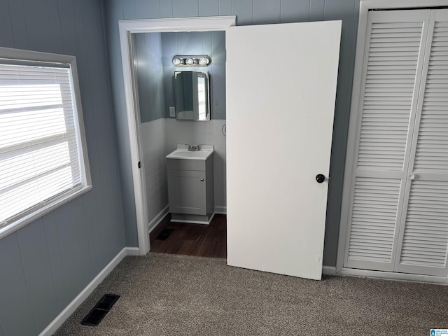 hall featuring wooden walls, sink, and dark carpet