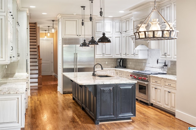 kitchen featuring light stone counters, a center island with sink, pendant lighting, and premium appliances