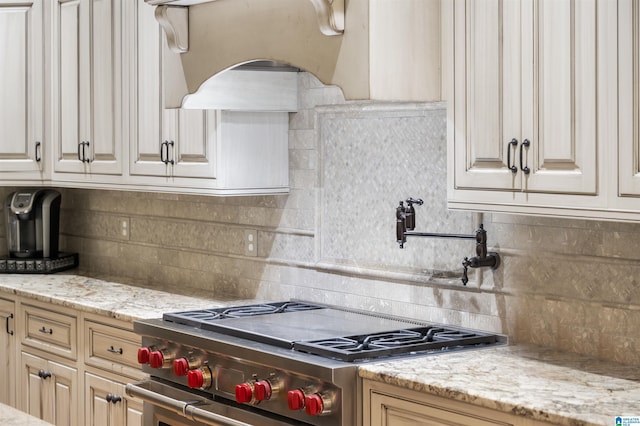 kitchen with high end range, light stone countertops, backsplash, ventilation hood, and cream cabinets