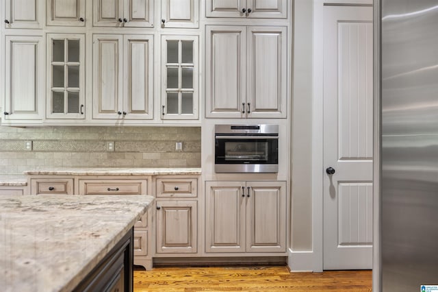 kitchen featuring tasteful backsplash, light stone countertops, stainless steel appliances, and light hardwood / wood-style floors