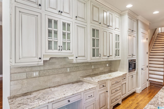 kitchen featuring oven, tasteful backsplash, light stone countertops, and light hardwood / wood-style flooring