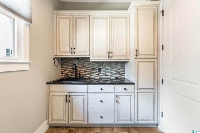 interior space with backsplash, cream cabinetry, sink, and dark stone counters