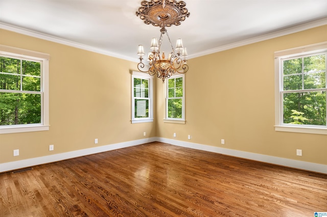 empty room featuring wood-type flooring, ornamental molding, and an inviting chandelier