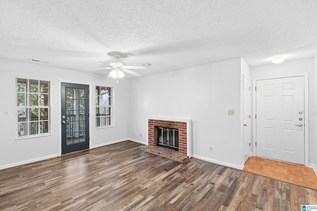 unfurnished living room featuring a fireplace, a textured ceiling, dark hardwood / wood-style floors, and ceiling fan