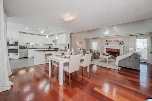 dining area featuring hardwood / wood-style floors, a textured ceiling, a brick fireplace, and ceiling fan