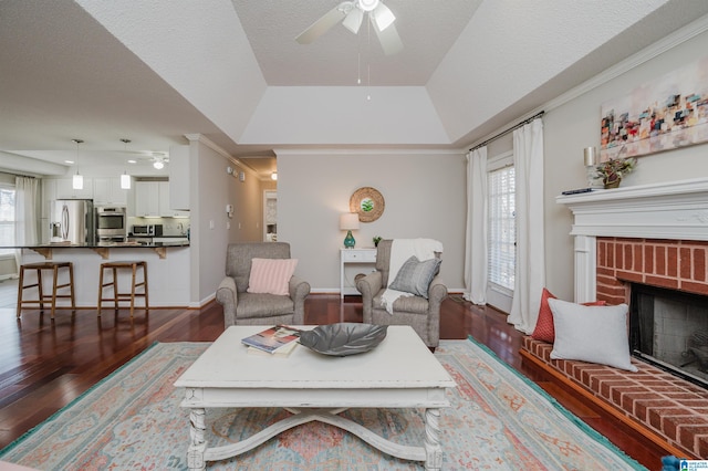 living room featuring dark wood-type flooring, a textured ceiling, a tray ceiling, a fireplace, and ornamental molding