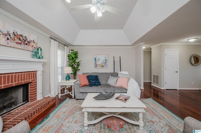 living room with crown molding, ceiling fan, a textured ceiling, a fireplace, and a tray ceiling