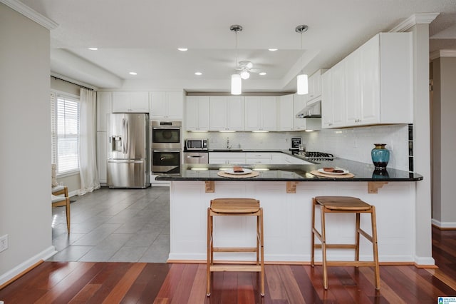 kitchen with stainless steel appliances, kitchen peninsula, decorative light fixtures, a kitchen bar, and white cabinets