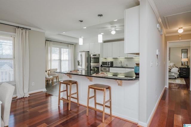 kitchen featuring pendant lighting, a breakfast bar, white cabinets, ornamental molding, and appliances with stainless steel finishes