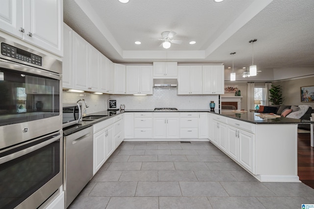 kitchen featuring kitchen peninsula, appliances with stainless steel finishes, white cabinetry, and hanging light fixtures