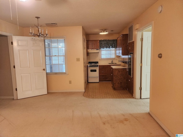 kitchen with sink, hanging light fixtures, a chandelier, light carpet, and white stove