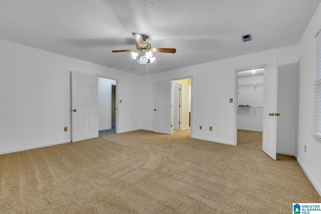 unfurnished bedroom with light carpet, a textured ceiling, ceiling fan, a spacious closet, and a closet