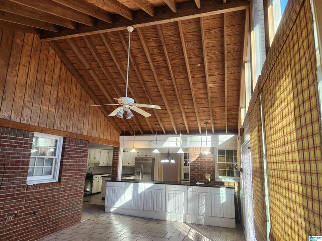 interior space featuring brick wall, pendant lighting, high vaulted ceiling, stainless steel fridge with ice dispenser, and wood walls