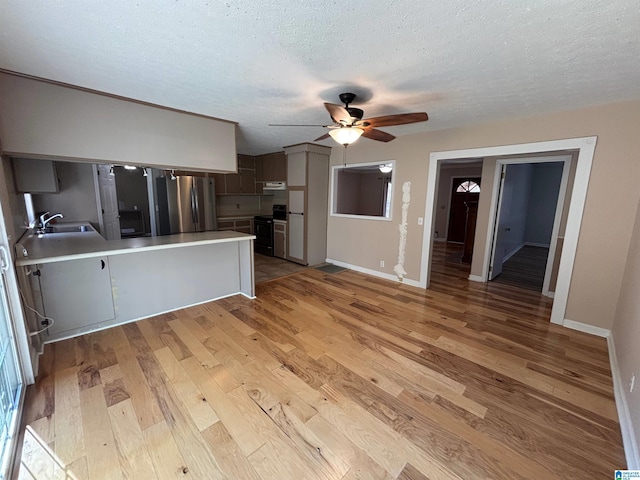 kitchen with stainless steel refrigerator, sink, kitchen peninsula, extractor fan, and light wood-type flooring