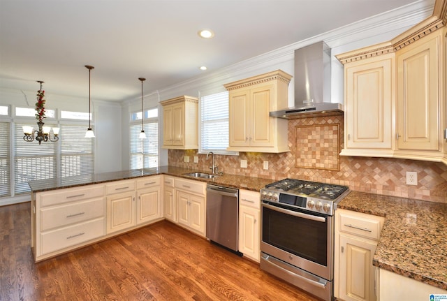 kitchen featuring kitchen peninsula, appliances with stainless steel finishes, wall chimney exhaust hood, sink, and hanging light fixtures