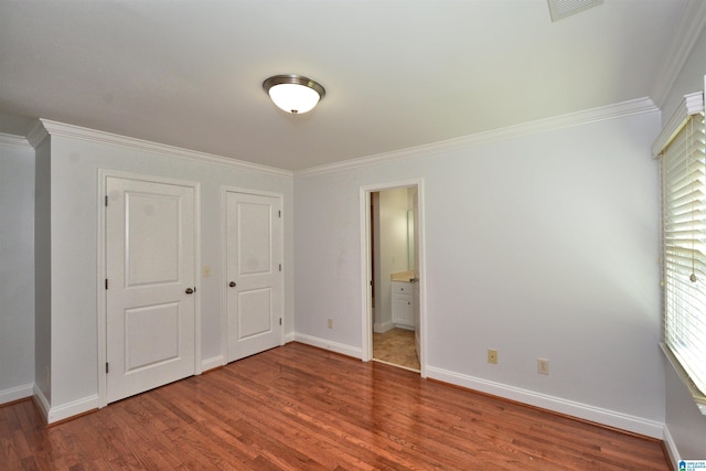 unfurnished bedroom featuring wood-type flooring, crown molding, connected bathroom, and a closet