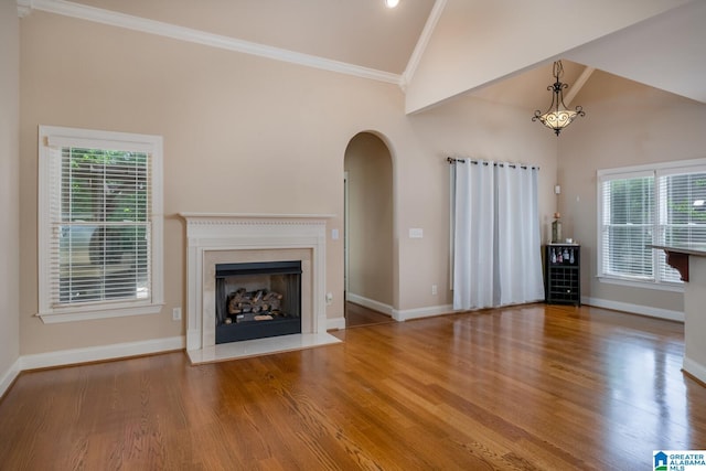 unfurnished living room featuring wood-type flooring, vaulted ceiling, a healthy amount of sunlight, and crown molding