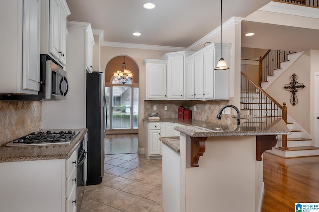 kitchen with hanging light fixtures, kitchen peninsula, a kitchen bar, white cabinets, and appliances with stainless steel finishes