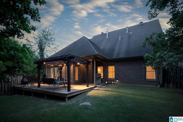 back house at dusk with a deck, a pergola, and a yard