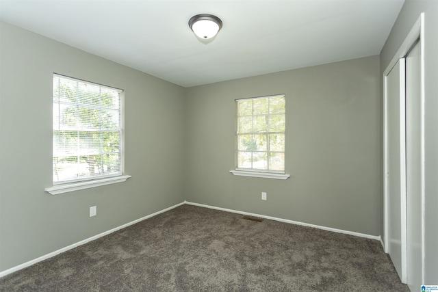 unfurnished bedroom with dark carpet, multiple windows, and a closet