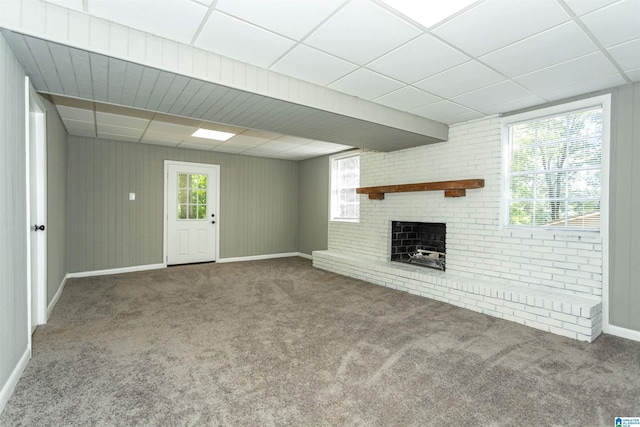 unfurnished living room featuring carpet, a drop ceiling, and a brick fireplace