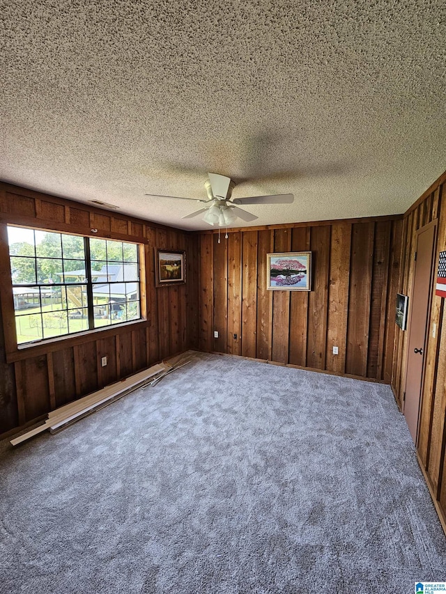 unfurnished room featuring ceiling fan, wooden walls, carpet, and a textured ceiling