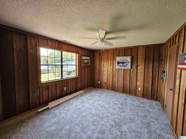 carpeted empty room with ceiling fan, wood walls, baseboard heating, and a textured ceiling