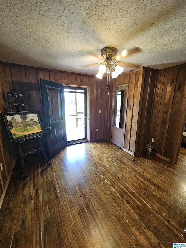 interior space with ceiling fan, wood walls, and dark hardwood / wood-style flooring