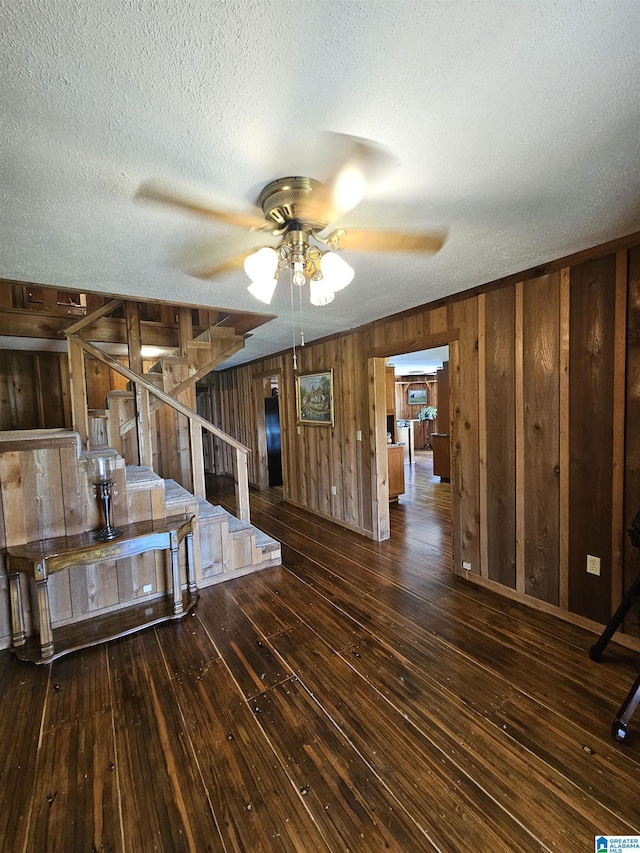 interior space featuring a textured ceiling, ceiling fan, dark hardwood / wood-style flooring, and wood walls