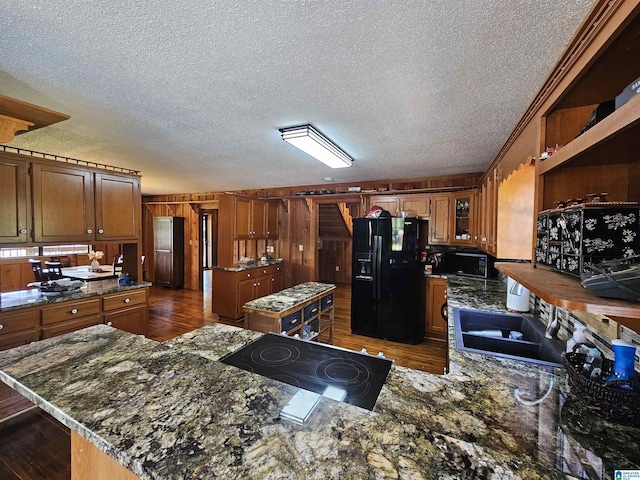 kitchen featuring a textured ceiling, wooden walls, sink, black appliances, and a kitchen island