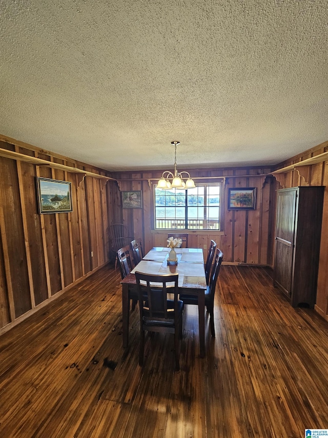 dining area with a textured ceiling, dark wood-type flooring, wooden walls, and a chandelier