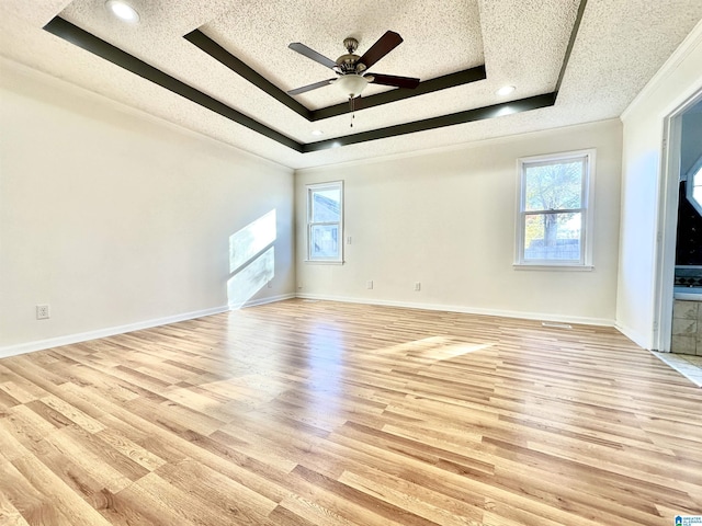 unfurnished living room featuring ceiling fan, light wood-type flooring, a textured ceiling, and a tray ceiling