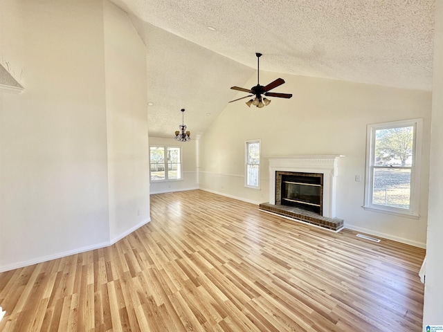 unfurnished living room featuring high vaulted ceiling, ceiling fan with notable chandelier, light wood-type flooring, a textured ceiling, and a fireplace