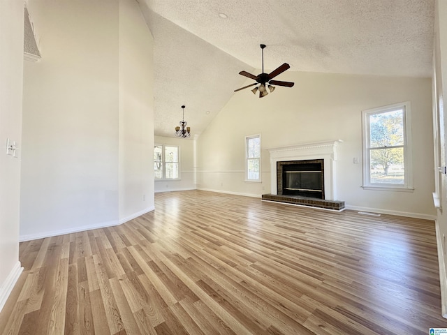 unfurnished living room featuring ceiling fan with notable chandelier, light wood-type flooring, a textured ceiling, and high vaulted ceiling