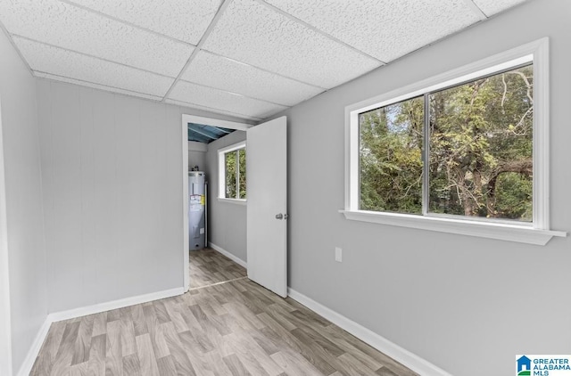 spare room with a paneled ceiling, water heater, and light wood-type flooring