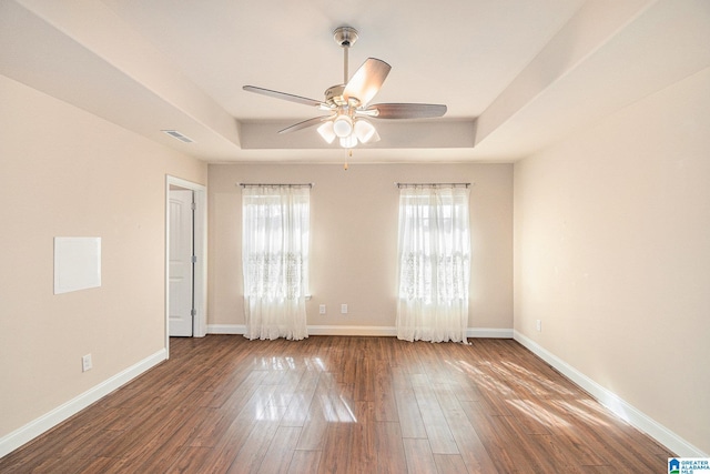 empty room featuring dark wood-type flooring, ceiling fan, and a raised ceiling