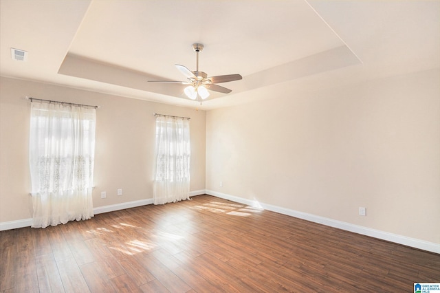 empty room featuring hardwood / wood-style flooring, ceiling fan, and a tray ceiling