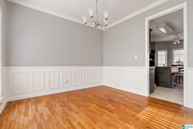 spare room featuring ceiling fan with notable chandelier, light wood-type flooring, and crown molding