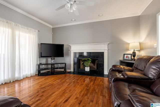 living room featuring a premium fireplace, ceiling fan, wood-type flooring, and ornamental molding