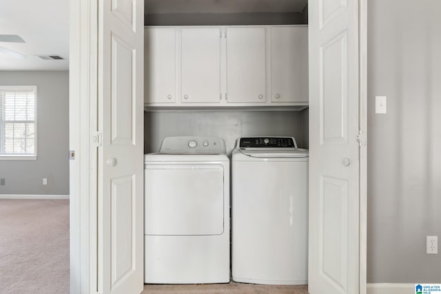 laundry room featuring washer and dryer, light carpet, and cabinets