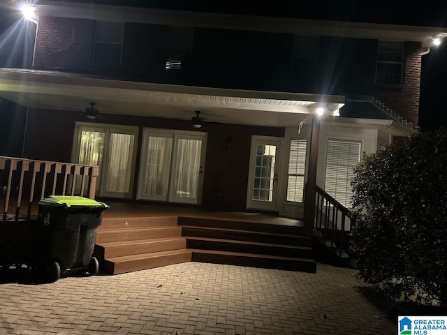 exterior entry at night featuring ceiling fan and a deck