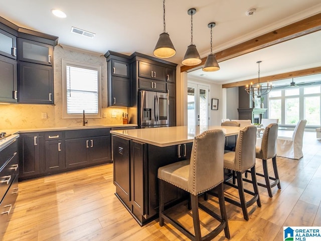 kitchen featuring a breakfast bar, a center island, crown molding, stainless steel refrigerator with ice dispenser, and hanging light fixtures