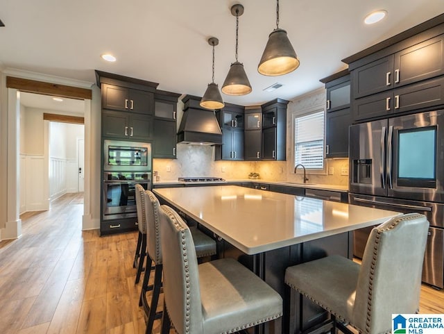 kitchen featuring sink, pendant lighting, a kitchen island, custom range hood, and appliances with stainless steel finishes