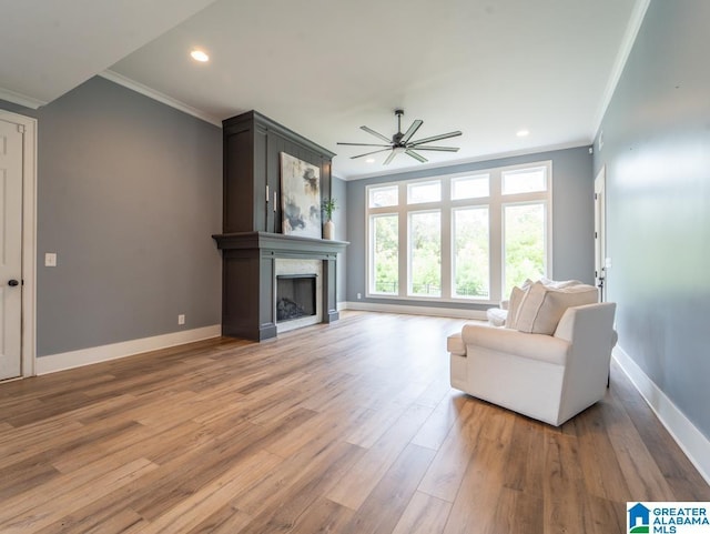 living room with hardwood / wood-style flooring, ceiling fan, ornamental molding, and a fireplace